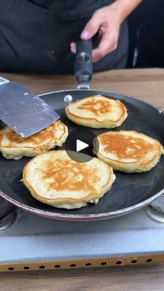 pancakes being cooked in a pan with a spatula on the side and someone using a knife to cut them