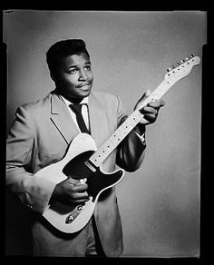 a black and white photo of a man in a suit holding an electric guitar with his right hand