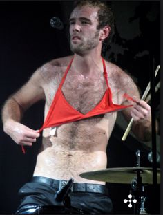 a shirtless man with no shirt on holding drums in front of his face and wearing a red triangle