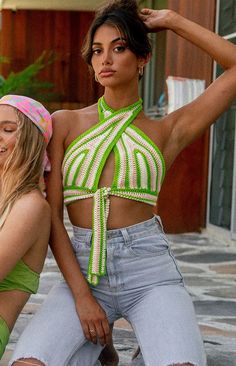 two women sitting on the ground with their arms around each other and one wearing a green halter top