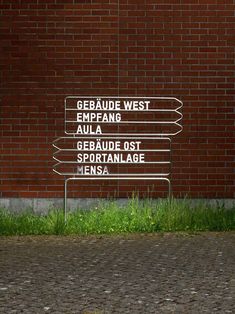 a street sign in front of a brick wall with grass growing on the ground below it