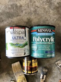 two cans of paint sitting on top of a floor next to other paints and brushes