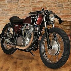 a red and black motorcycle parked in front of a brick wall next to a wooden floor