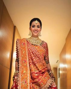 a woman in an orange and red bridal outfit posing for the camera with her hands on her hips