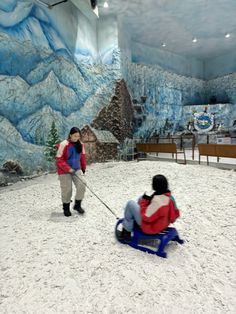 two people on sleds in an indoor area with snow and mountains painted on the walls