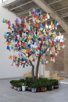 a tree with many colorful butterflies on it's trunk in a room filled with potted plants