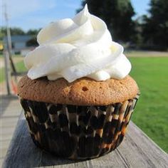 a cupcake with whipped cream on top sitting on a wooden table in the park