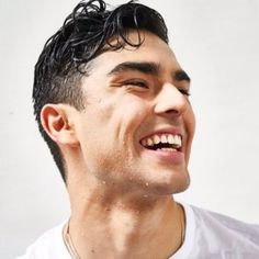 a man smiling and wearing a white t - shirt with his hair in the wind