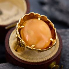 an orange stone ring sitting on top of a wooden display stand in front of a box