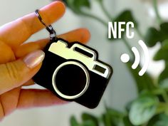 a hand holding a camera keychain with the words nfl on it and a plant in the background