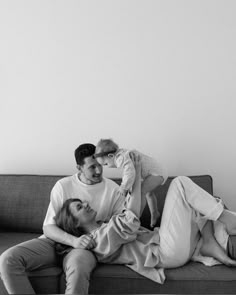 a man and woman sitting on top of a couch with a baby in their lap