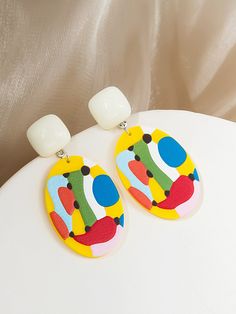 a pair of colorful earrings sitting on top of a white table next to a lamp