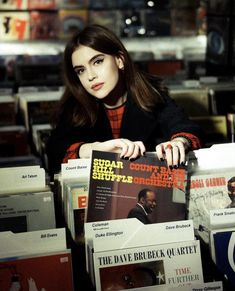 a woman sitting at a table with some records in front of her and holding one of the covers