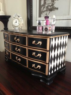 a black and gold dresser sitting on top of a wooden table next to a mirror