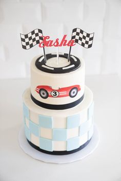 a cake decorated with a racing car and checkerboard pattern on the side, topped with two flags