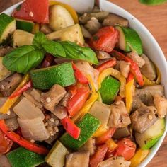 a white bowl filled with mixed vegetables on top of a wooden table next to a spoon