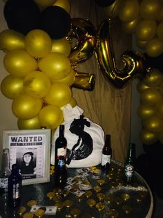 a table topped with lots of gold balloons and bottles of wine next to a bunch of black and white balloons