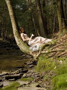 a woman sitting on top of a tree next to a river in the woods with words written