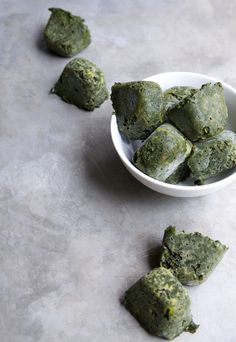 small white bowl filled with green food on top of a table next to smaller pieces of broccoli