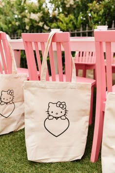 hello kitty bags sitting on the grass next to pink wooden chairs and table set up for an outdoor party