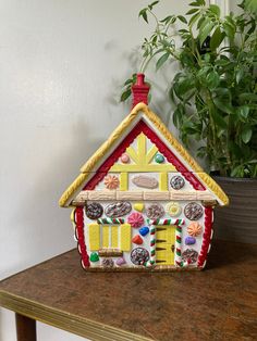 a house shaped cookie box sitting on top of a table next to a potted plant