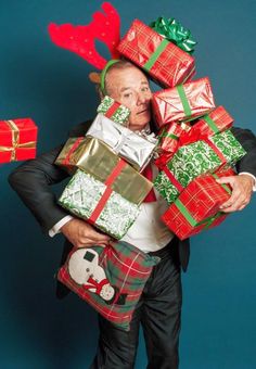 a man in a suit carrying many wrapped presents on his back with reindeer antlers