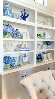 a white chair sitting in front of a bookshelf filled with blue and white vases