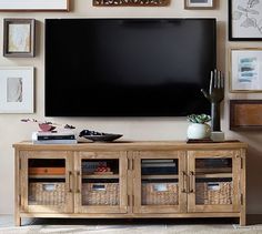 a flat screen tv mounted to the side of a wooden entertainment center with baskets underneath it