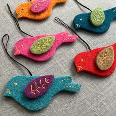 four felt bird ornaments are sitting on a table top, each with different colors and designs