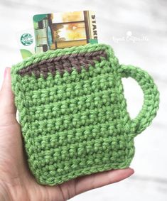 a hand holding a green crocheted coffee cup with a credit card in it