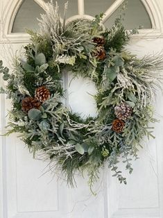 a wreath with pine cones and greenery is hanging on the front door to welcome guests