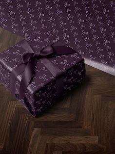 a purple gift box with a bow on it sitting on a wooden floor next to a wall