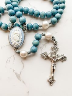 "This handcrafted, beautiful, and unique Catholic rosary is made with 8mm dyed blue beads and 10mm natural pearl beads. The beads are strung and knotted on micro cord (the slimmest type of paracord!) for durability. The cameo rosary center depicts our Lady of Guadalupe. The crucifix is 2 inches in length and was made in Italy. This rosary is about 14 inches in length and is lightweight and easy to carry with you so you can \"pray without ceasing.\" Each rosary from Refuge Rosaries is carefully p Cheap Handmade Spiritual Rosary, Affordable Blue Rosary Bracelet As Gift, Rosary Case, Rosary Jewelry, Rosary Beads Catholic, Praying The Rosary, Pray Without Ceasing, Catholic Rosary, Our Lady Of Guadalupe