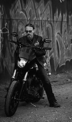 a man sitting on top of a motorcycle next to a wall with grafitti