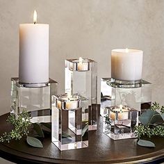 three candles sitting on top of a table next to some glass containers with greenery