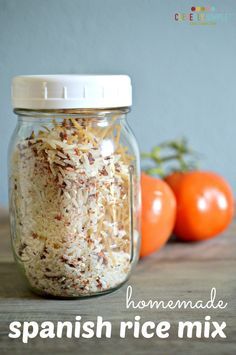 a glass jar filled with shredded cheese next to two tomatoes on a wooden table and another orange in the background