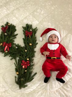 a baby is laying next to a christmas letter made out of fake fir branches and decorations