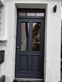 the front door of a white house with dark blue trim and glass panels on it