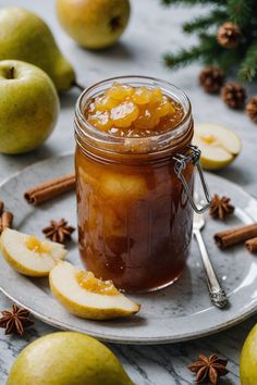 an apple jam in a glass jar on a plate with apples and cinnamons around it