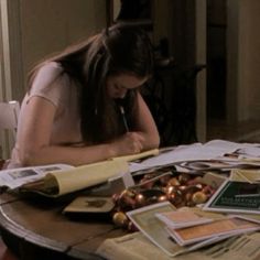 a woman sitting at a table with papers and pens in her hand, writing on a piece of paper