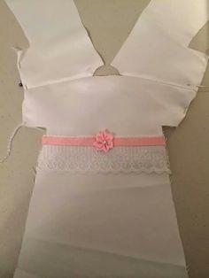 a piece of white cloth with pink ribbon and flower on the side, sitting on top of a table