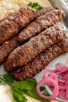 some meat sticks are on a plate with onion rings and cilantros next to it