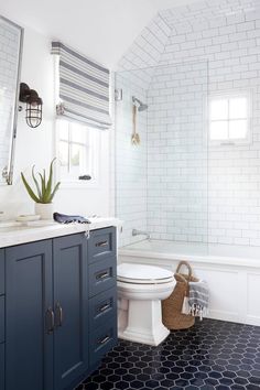 a white toilet sitting next to a bath tub in a bathroom with blue cabinets and drawers