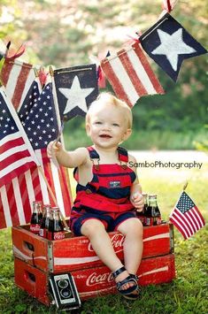 a baby sitting on top of an old crate with american flags and coke bottles in it