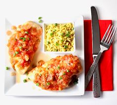 a white plate topped with meat covered in sauce and rice next to a knife and fork