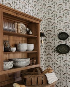 a wooden shelf filled with dishes next to a wallpaper covered in floral print paper