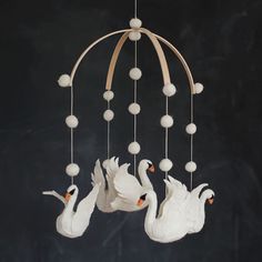 three white swans are hanging from a wooden chandelier with balls on the strings