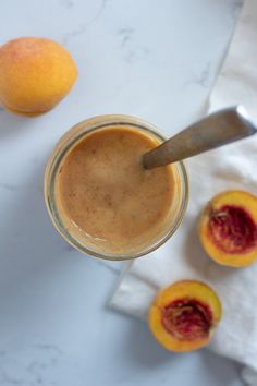 a glass jar filled with liquid next to two peaches on a white tablecloth