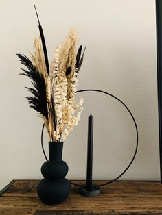 dried flowers in a black vase on a wooden table next to a candle holder with two candles