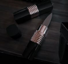 a knife and some other items on a wooden table next to a black box with gold trim